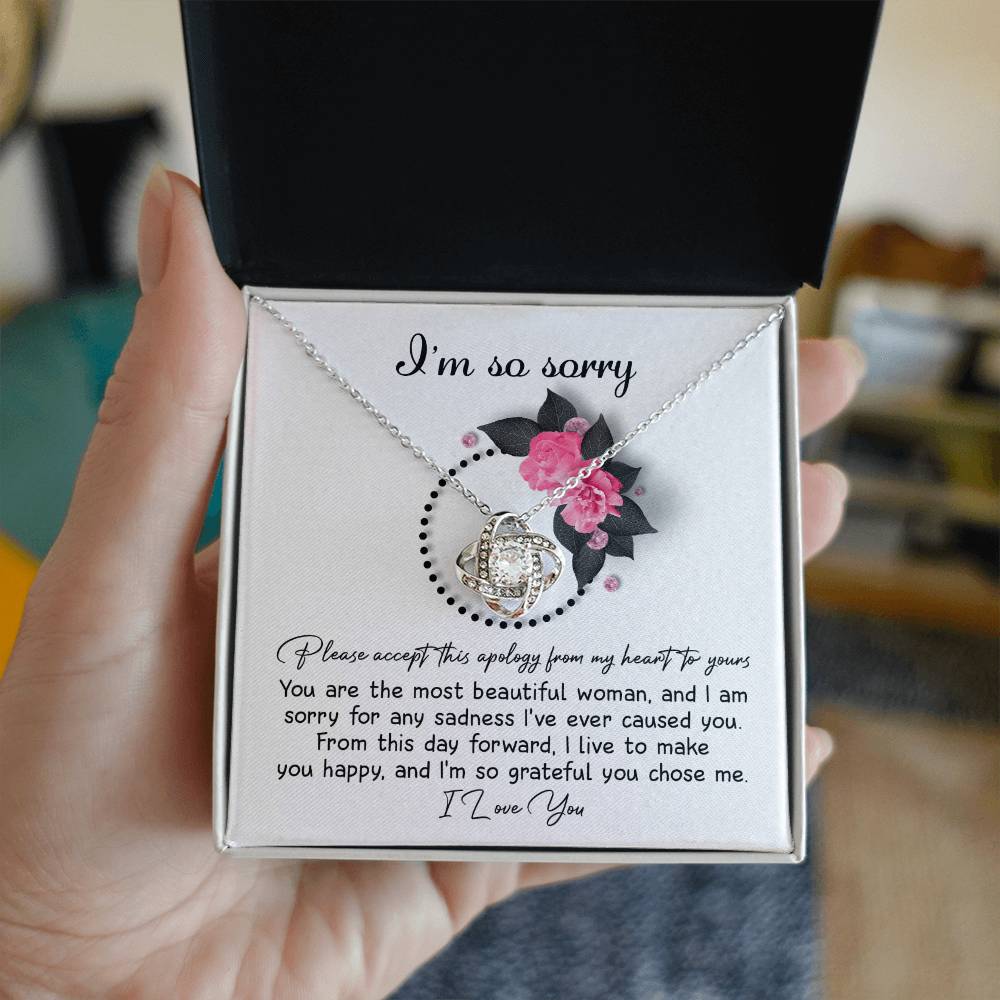 The Sorry-Make You Happy - Love Knot Necklace features a heart-shaped pendant adorned with cubic zirconia crystals, presented in a box decorated with pink flowers and the heartfelt text "I'm so sorry" at the top.