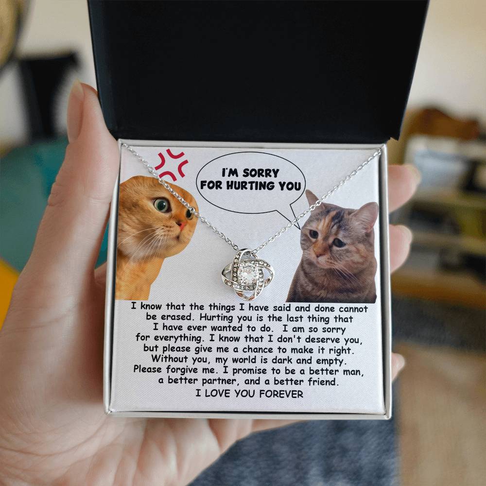 The Sorry-Make It Right - Love Knot Necklace showcases a heartfelt note adorned with two cats, one angry and the other sad. The note conveys remorse with the message, "I'm sorry for hurting you," alongside a promise to improve. Enhanced by cubic zirconia crystals and personalized for an intimate touch, it reads "I LOVE YOU FOREVER.