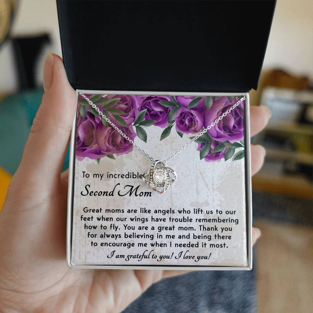 Hand holding an open gift box displaying the "To Bonus Mom, Grateful For You - Love Knot Necklace" adorned with cubic zirconia crystals. The message inside expresses gratitude and appreciation to a "Bonus Mom" with supportive and loving words, making it the perfect personalized gift.