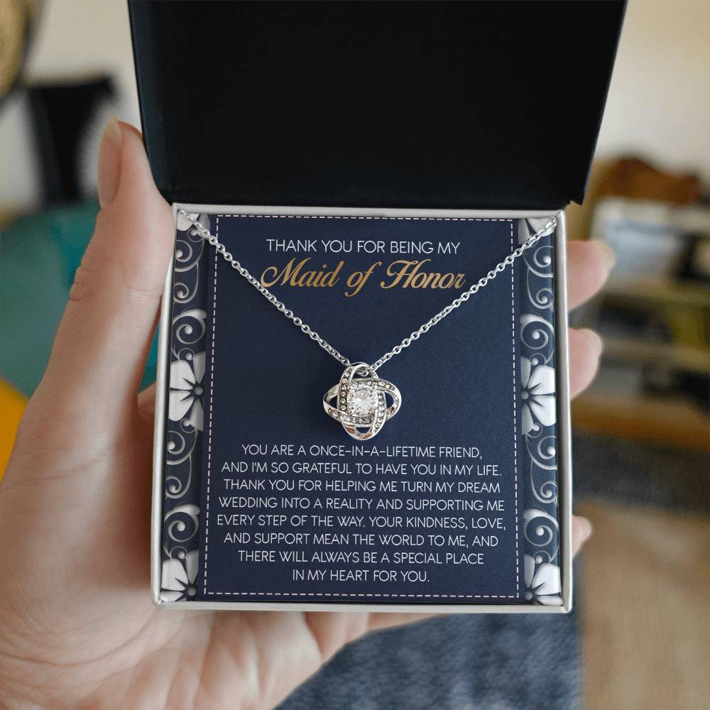 The "To Maid of Honor, World To Me - Love Knot Necklace" features a heart-shaped pendant adorned with Cubic Zirconia Crystals. It comes beautifully packaged in a box that includes an inscribed thank-you note, expressing heartfelt gratitude to the Maid of Honor, making it a perfect personalized gift.