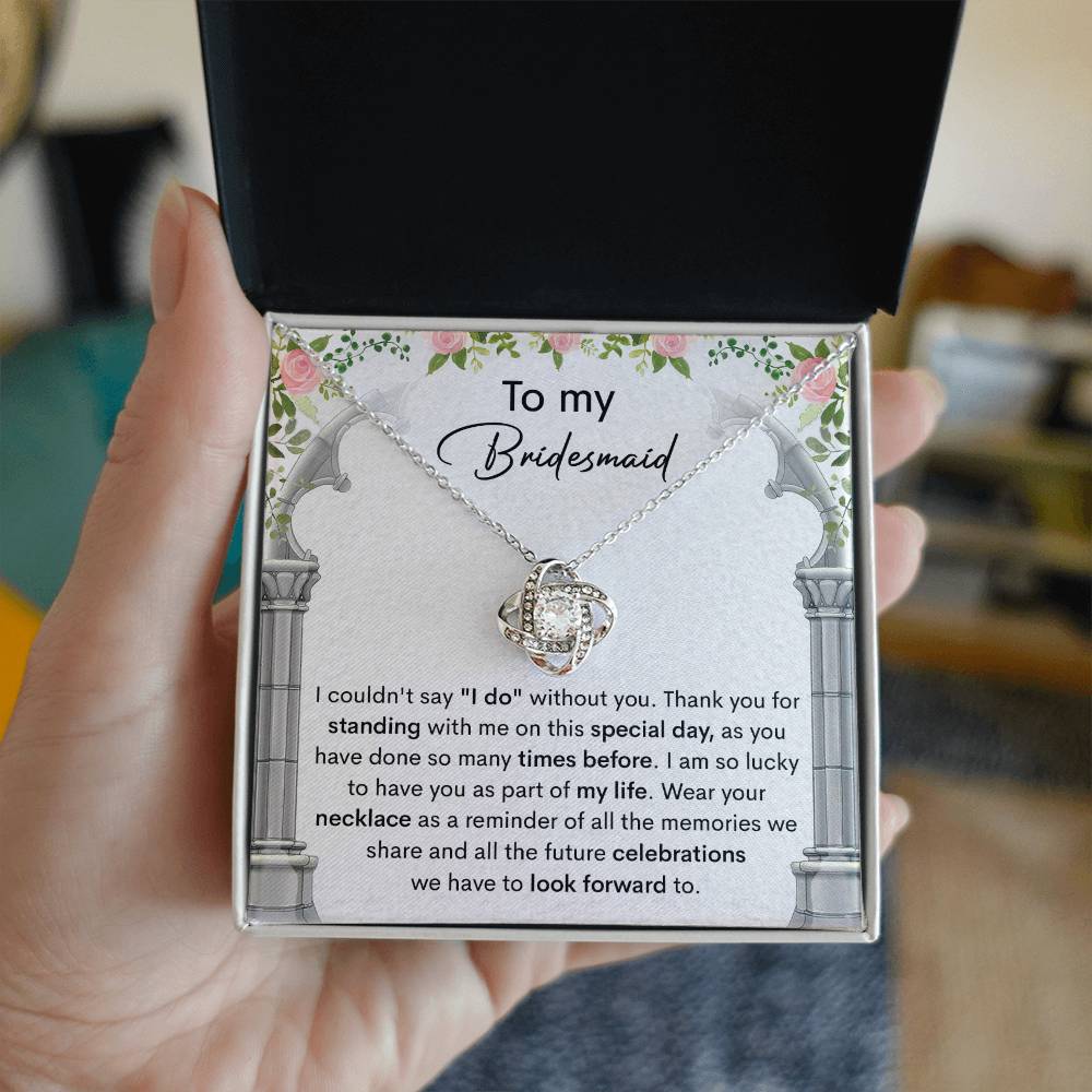 A personalized gift, the *To My Bridesmaid, Standing With Me - Love Knot Necklace* with cubic zirconia crystals, is displayed on a card that expresses gratitude to a bridesmaid, highlighting the importance of her support on the special day.