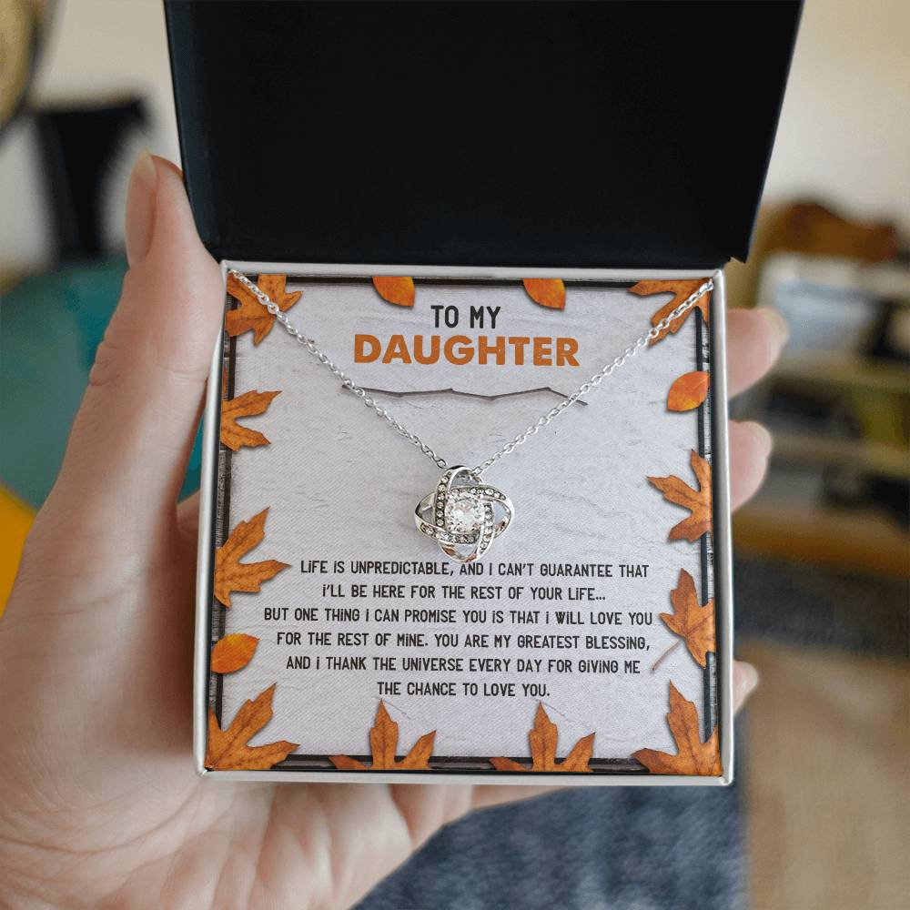 A hand holds an open jewelry box displaying the Daughter-My Greatest Blessing - Love Knot Necklace adorned with cubic zirconia crystals. The box's lid reads "To My Daughter" above a heartfelt message, symbolizing the unbreakable bond between them.