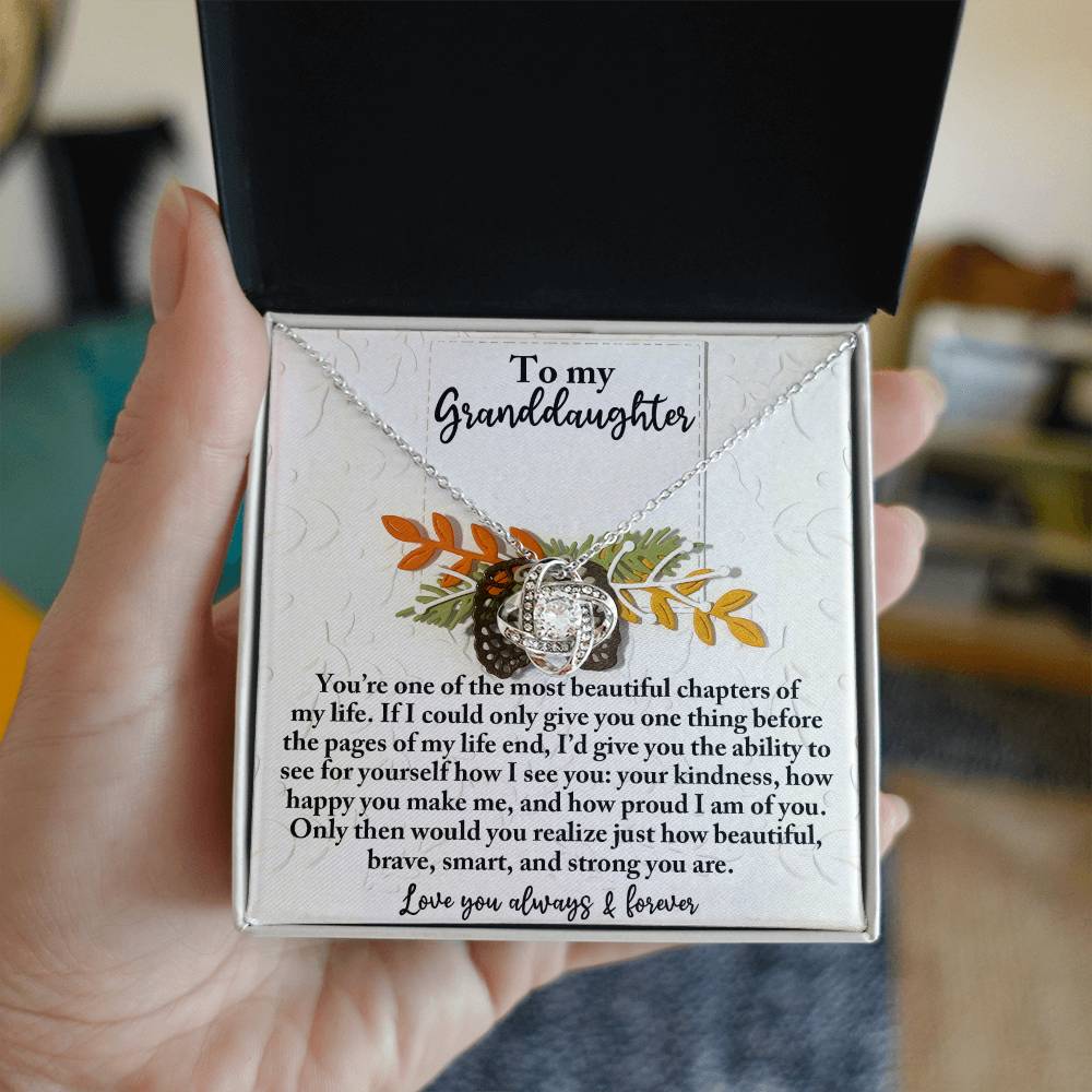 An open box is held, revealing the stunning Granddaughter-How Beautiful - Love Knot Necklace with its sparkle accentuated by cubic zirconia, paired with a heartfelt message for a cherished granddaughter.
