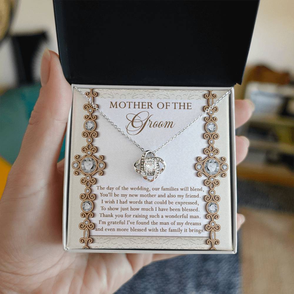 To Mom Of Groom, New Mother - Love Knot Necklace with an interlocking heart pendant, adorned with cubic zirconia crystals, on a card reading: “Mother of the Groom” and a heartfelt message appreciating the groom's mother. Available in white gold or yellow gold finish.
