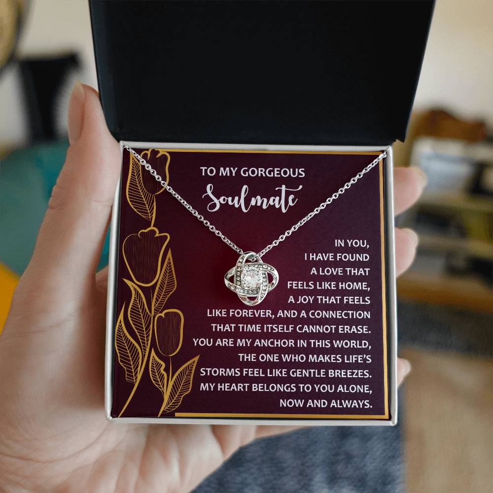 A person holds an open jewelry box showcasing the Soulmate-Gentle Breezes - Love Knot Necklace with a card expressing love to a "gorgeous soulmate," making it a personalized gift that speaks from the heart.