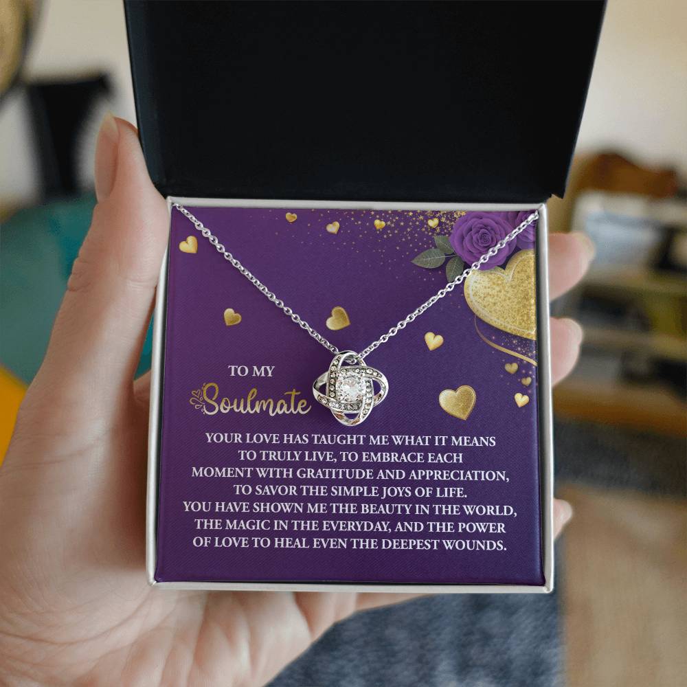 A hand holds an open gift box with a stunning Soulmate-Joys Of Life - Love Knot Necklace. The inside lid conveys a heartfelt message about love and soulmates, making it the perfect personalized gift for someone special.