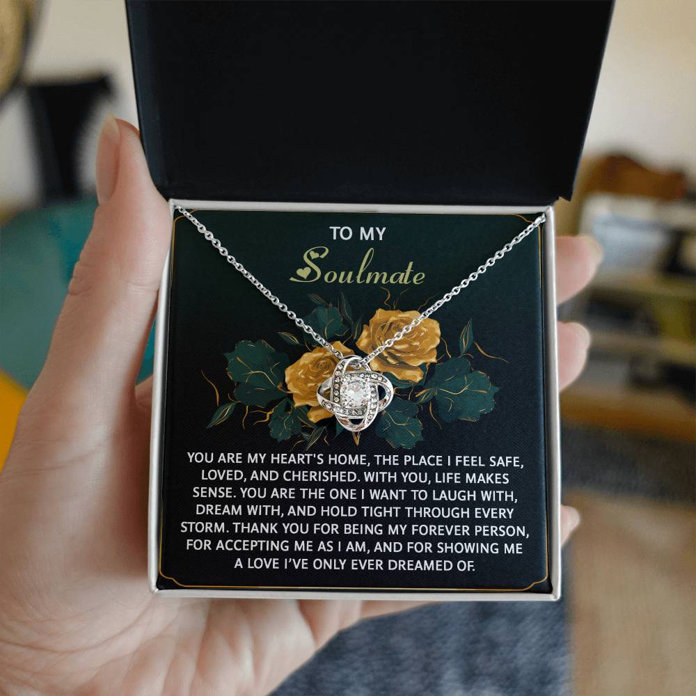 A hand holds an open Soulmate-Forever Person - Love Knot Necklace box, crafted in 14k white gold with sparkling cubic zirconia. The inside lid has "To My Soulmate" text and a heartfelt message, surrounded by illustrations of yellow roses.