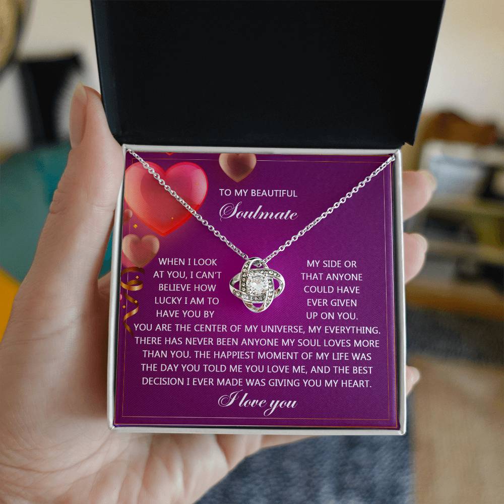 The Soulmate-My Soul Love Knot Necklace, featuring a silver interlocking pendant with cubic zirconia crystals, arrives in a gift box. The interior lid shows a romantic message on a purple background with heart graphics, making it an ideal personalized gift.