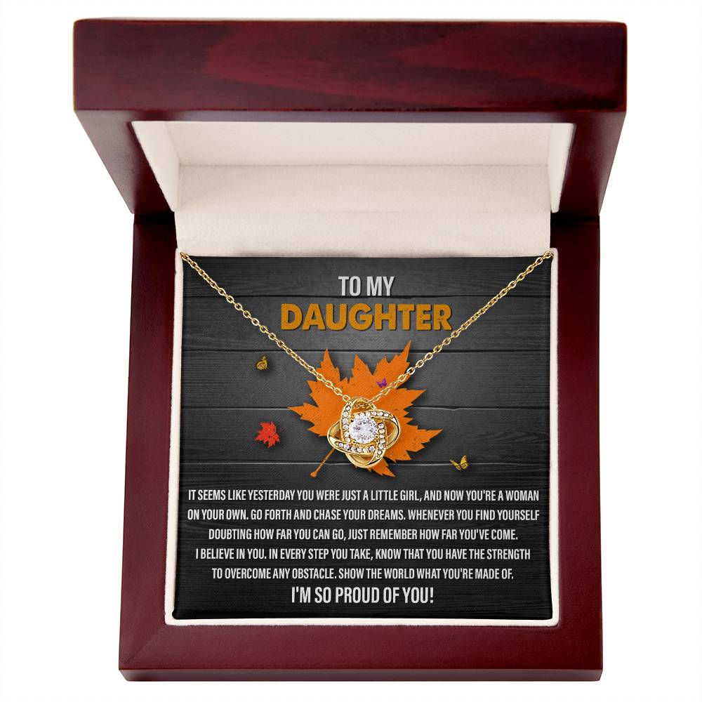 Presenting the Daughter-You Can Go - Love Knot Necklace: a personalized gift nestled inside a wooden box, featuring a stunning Love Knot Necklace adorned with cubic zirconia crystals. This heartfelt present is complemented by a touching note that begins with "To my daughter" and includes an inspiring message, beautifully decorated with fall leaves.