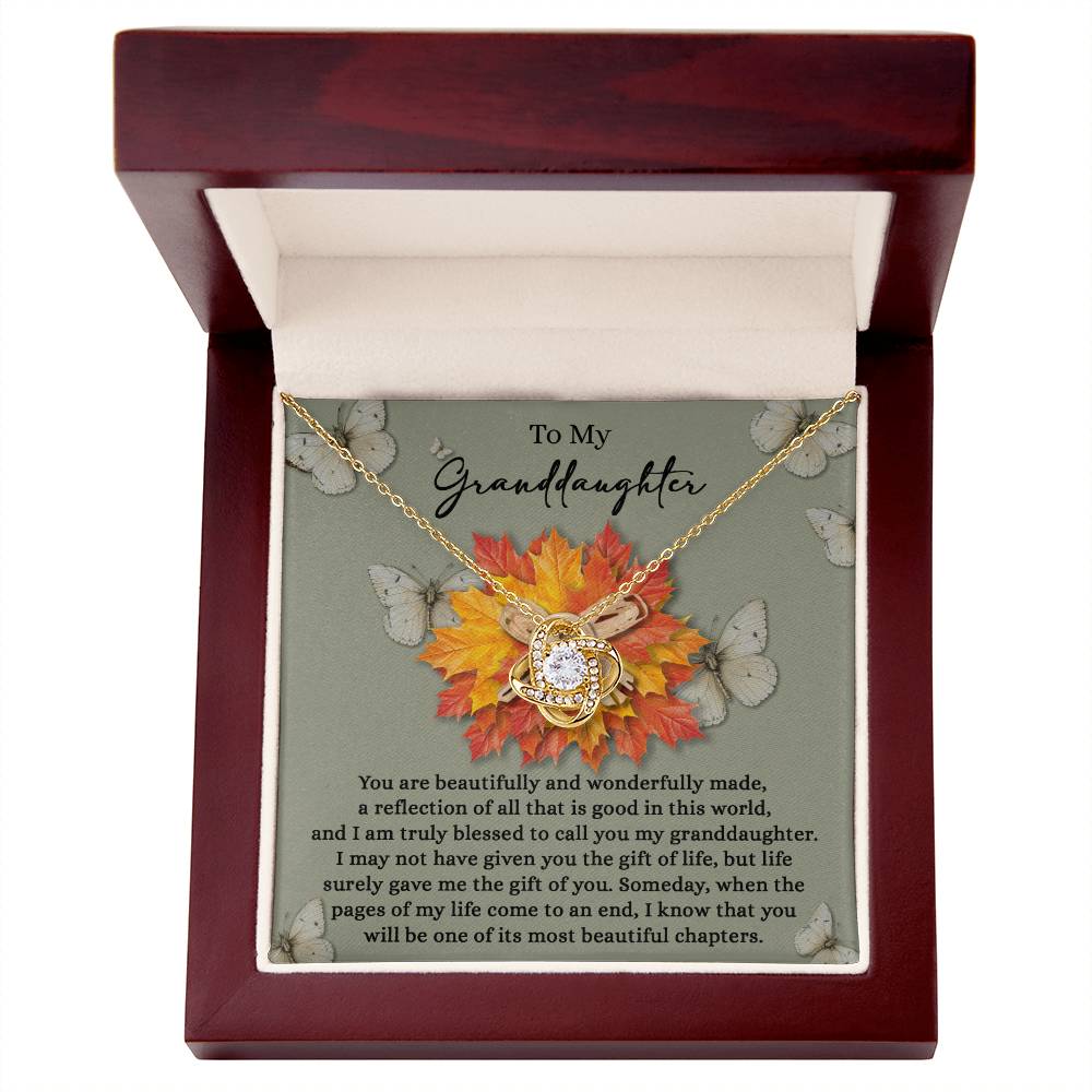 The Granddaughter-Gift Of You - Love Knot Necklace, featuring a dazzling pendant embellished with Cubic Zirconia Crystals, is elegantly placed in a wooden box. It comes with a touching message for your granddaughter, amid a backdrop of autumn leaves and butterflies.