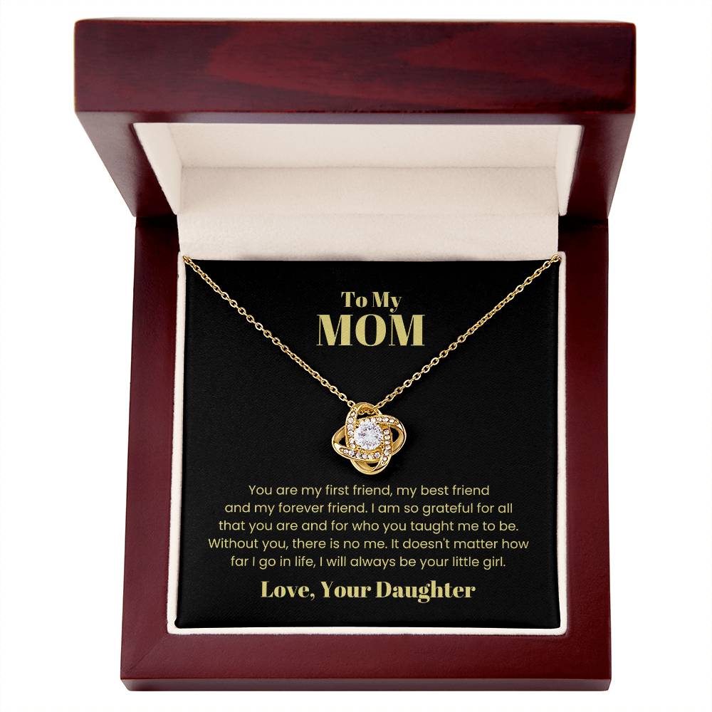 The "To My Mom, You Are My First Friend - Love Knot Necklace" features a gold pendant centered with a cubic zirconia crystal, beautifully presented inside an open gift box. The box's interior bears a heartfelt engraved message dedicated to "Mom" from "Your Daughter." This necklace is available in either a white gold or yellow gold finish.