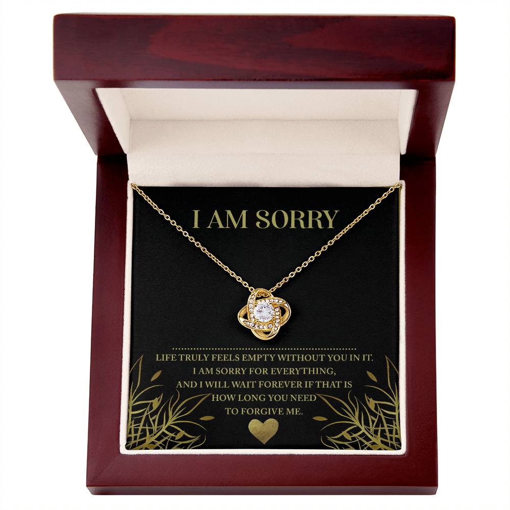 A "Sorry-Without You - Love Knot Necklace" adorned with sparkling cubic zirconia crystals is elegantly displayed in an open wooden box. Inside, a note reads, "I AM SORRY," accompanied by a heartfelt message of apology. This personalized gift captures the essence of sincerity and regret.