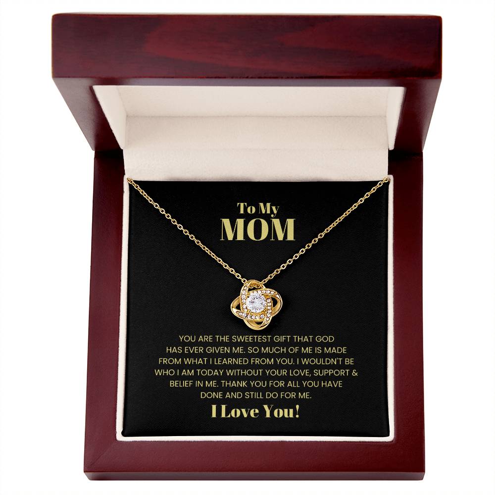 The "To My Mom, You Are The Sweetest Gift - Love Knot Necklace" with a gemstone pendant is elegantly presented inside a wooden box. The cover of the box reads: "To My MOM. I love you!" along with a heartfelt message in gold text on a black background, making it the perfect personalized gift adorned with premium cubic zirconia crystals.