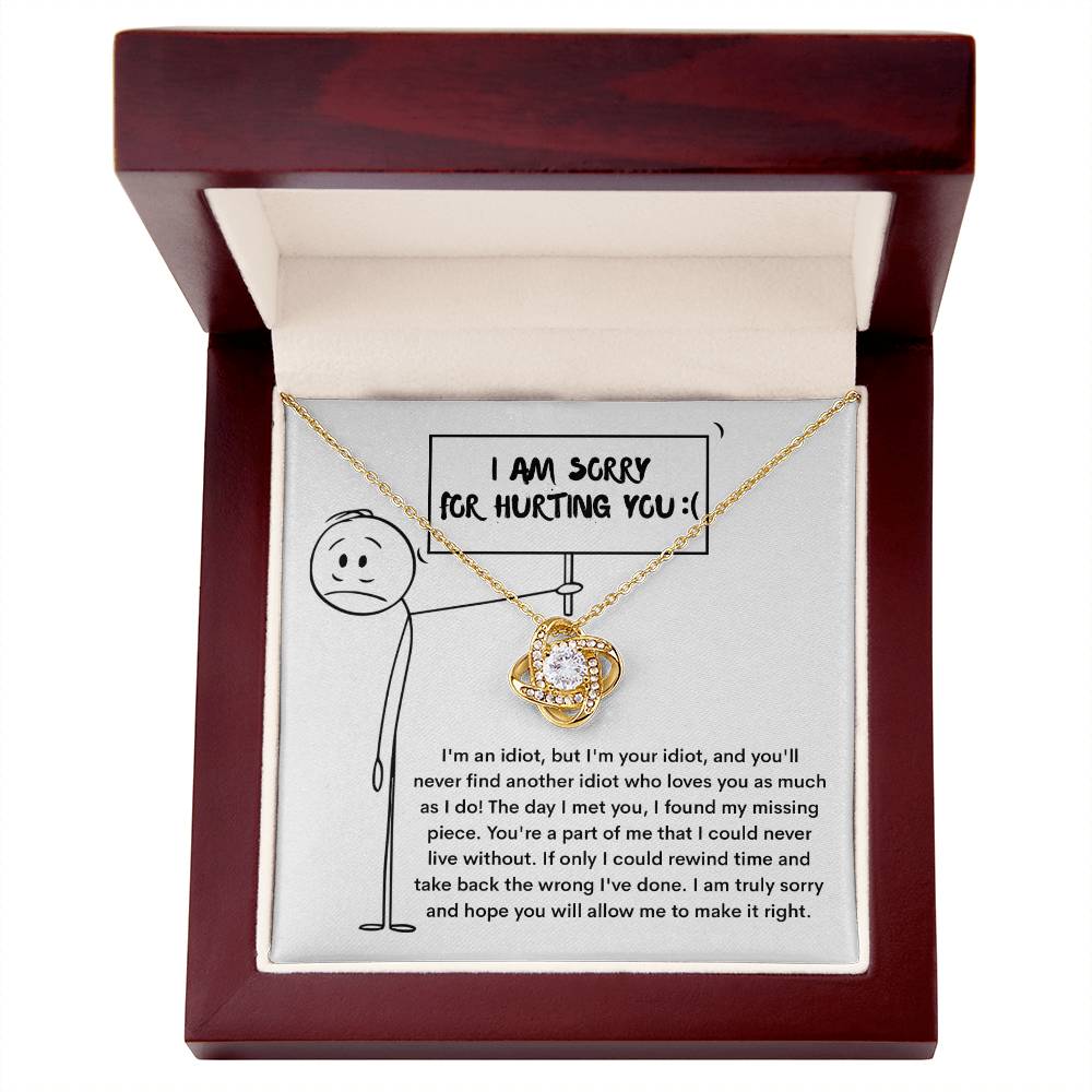 A classic gift, the Sorry-Missing Piece Love Knot Necklace features a large gemstone and is displayed in a wooden box. The box's interior shows a stick figure holding a sign that reads "I am sorry for hurting you," with text below offering an apology. Cubic zirconia crystals enhance this heartfelt gesture with an extra touch of elegance.