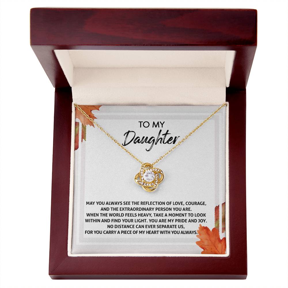 The "Daughter-Find Your Light - Love Knot Necklace," featuring a circular pendant adorned with cubic zirconia crystals and a stunning gold finish, is showcased in an open wooden box. Inside the box is a heartfelt message addressed to a daughter.
