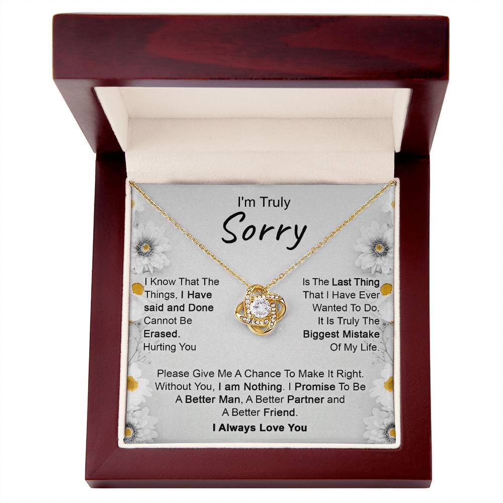The "I’m Truly Sorry - Love Knot Necklace," featuring a pendant adorned with cubic zirconia crystals, rests on a heartfelt message that reads, "I'm Truly Sorry." The text conveys remorse for past actions and a commitment to becoming a better person, partner, and friend. The background is decorated with delicate floral designs.