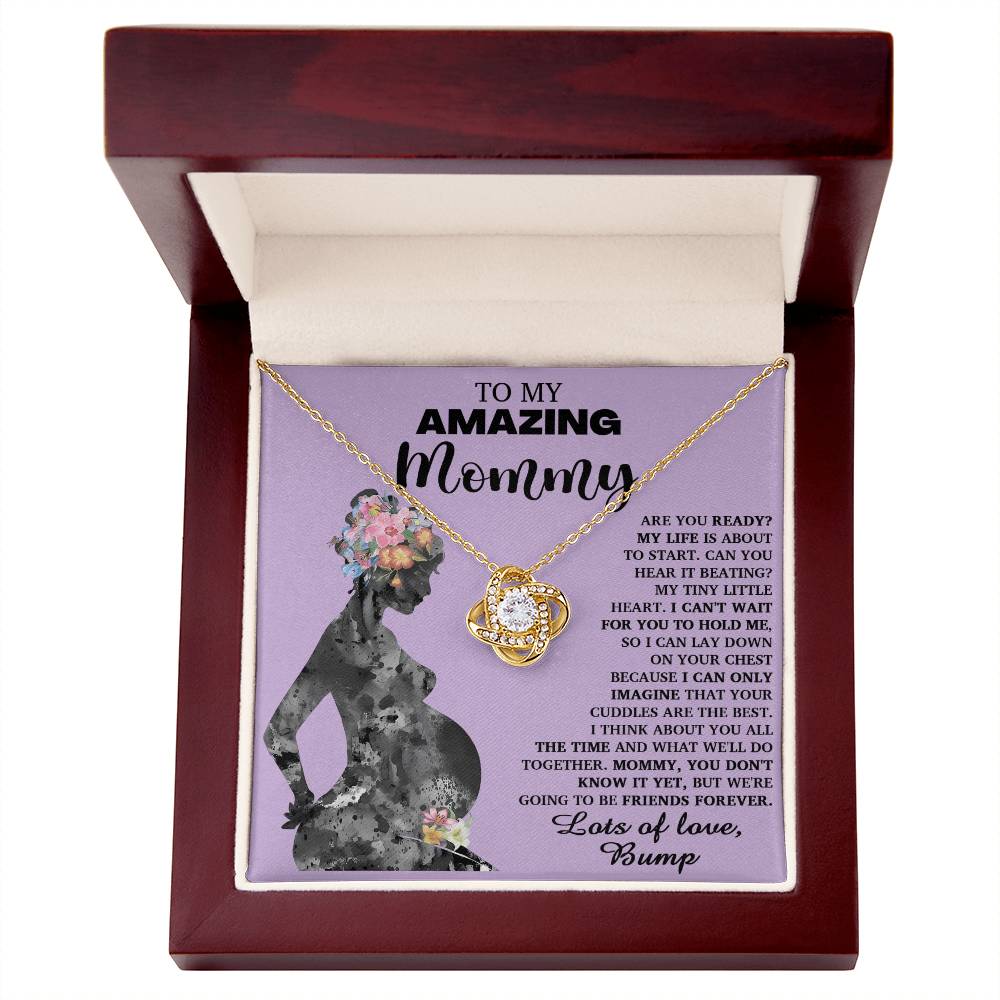 A "To Mom To Be, Tiny Little Heart - Love Knot Necklace" with premium cubic zirconia crystals is displayed in a red box. The lid features an illustration of a pregnant woman and a heartfelt message addressed to "Mommy" from "Bump," symbolizing the unbreakable bond between mother and child.