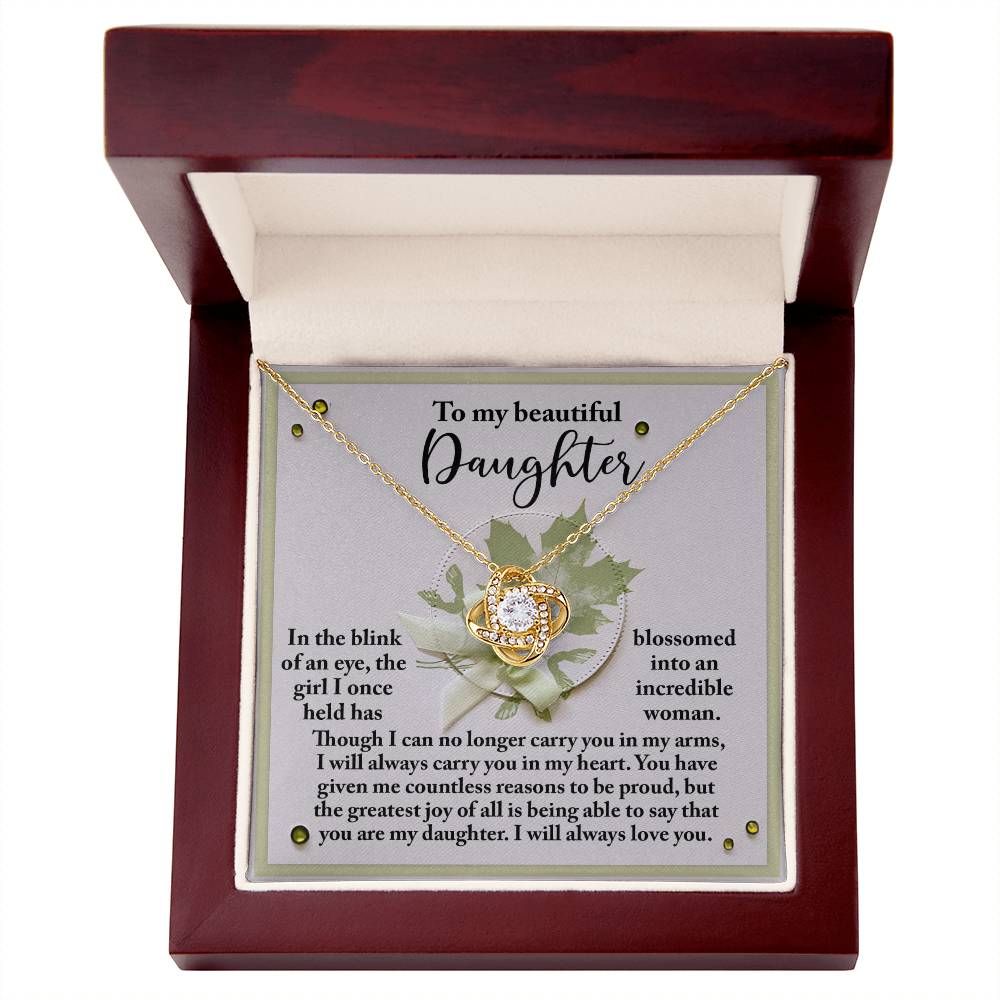 The "Daughter-Incredible Woman - Love Knot Necklace" features a circular pendant adorned with cubic zirconia crystals and comes in a wooden box with a white interior lining. Inside, a heartfelt message addresses the daughter, expressing love and pride from the sender. The pendant is elegantly crafted in 14k white gold.