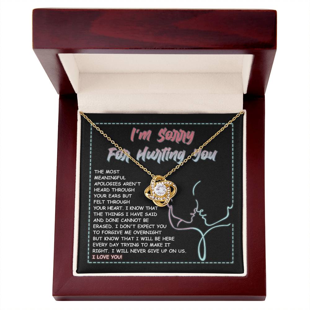 A 14k white gold Sorry-Never Give Up - Love Knot Necklace with an interlocked pendant set with cubic zirconia crystals sits on a note that reads, "I'm sorry for hurting you," accompanied by an apology message expressing regret, commitment to make things right, and affirming love.