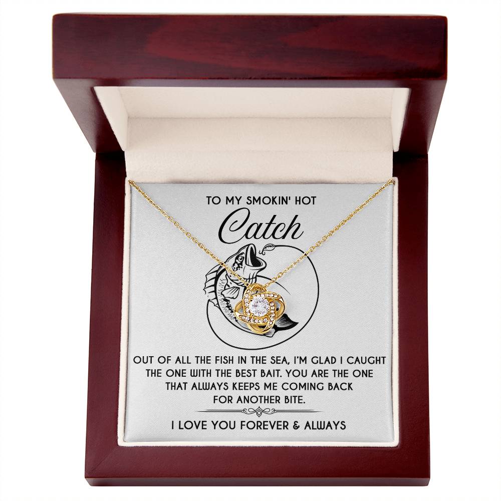 The Soulmate-Another Bite Love Knot Necklace comes in a wooden box with a romantic "To my smokin' hot catch" inscription. The gold-finished necklace adorned with cubic zirconia crystals includes a fish illustration and a heartfelt love message.