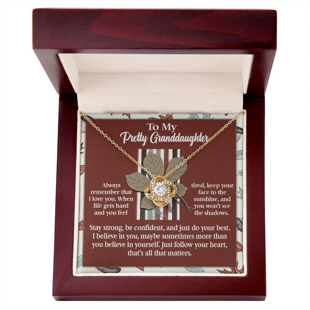 A captivating Granddaughter-See The Shadows - Love Knot Necklace, adorned with a circular pendant, is elegantly showcased in an open box. The lid includes an inspirational message meant for a granddaughter, beautifully embodying the essence of personalized jewelry.