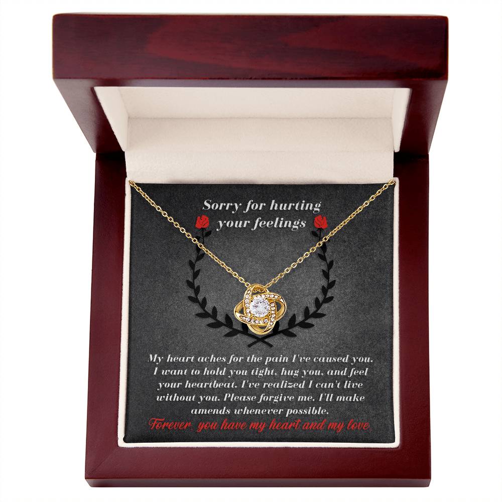 The Sorry-Make Amends - Love Knot Necklace, featuring a gold pendant adorned with cubic zirconia crystals, rests in a red and white jewelry box. The lid carries a heartfelt, personalized message apologizing for causing pain and asking for forgiveness, stating "Forever, you have my heart and my love.