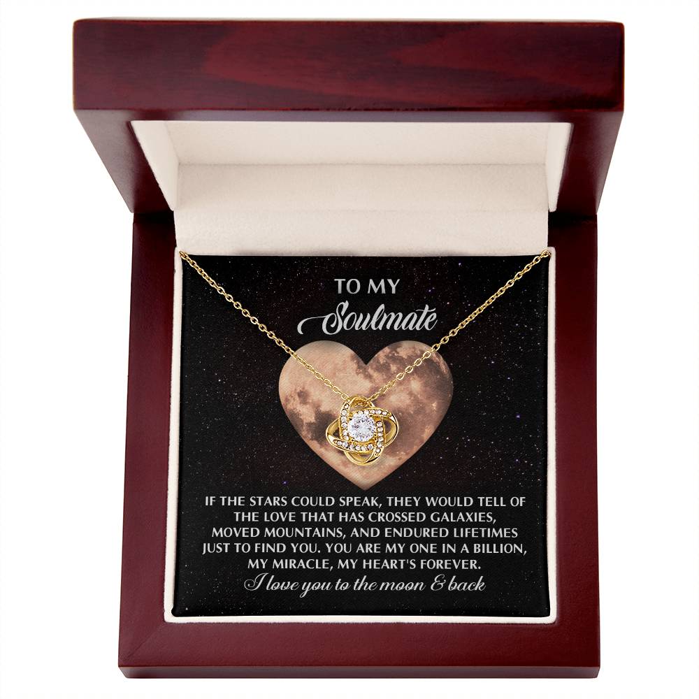 The Soulmate-Crossed Galaxies Love Knot Necklace, featuring a cubic zirconia-encrusted pendant, is elegantly presented in an open box with a heartfelt message set against a moonlit backdrop.