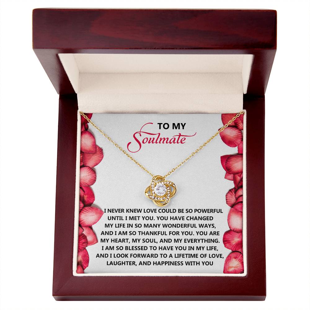 The Soulmate-Until I - Love Knot Necklace, featuring a gold central pendant, rests in a wooden box. The lid's interior displays a floral design and heartfelt text to "My Soulmate," symbolizing love, gratitude, and an unbreakable bond with shimmering cubic zirconia crystals.