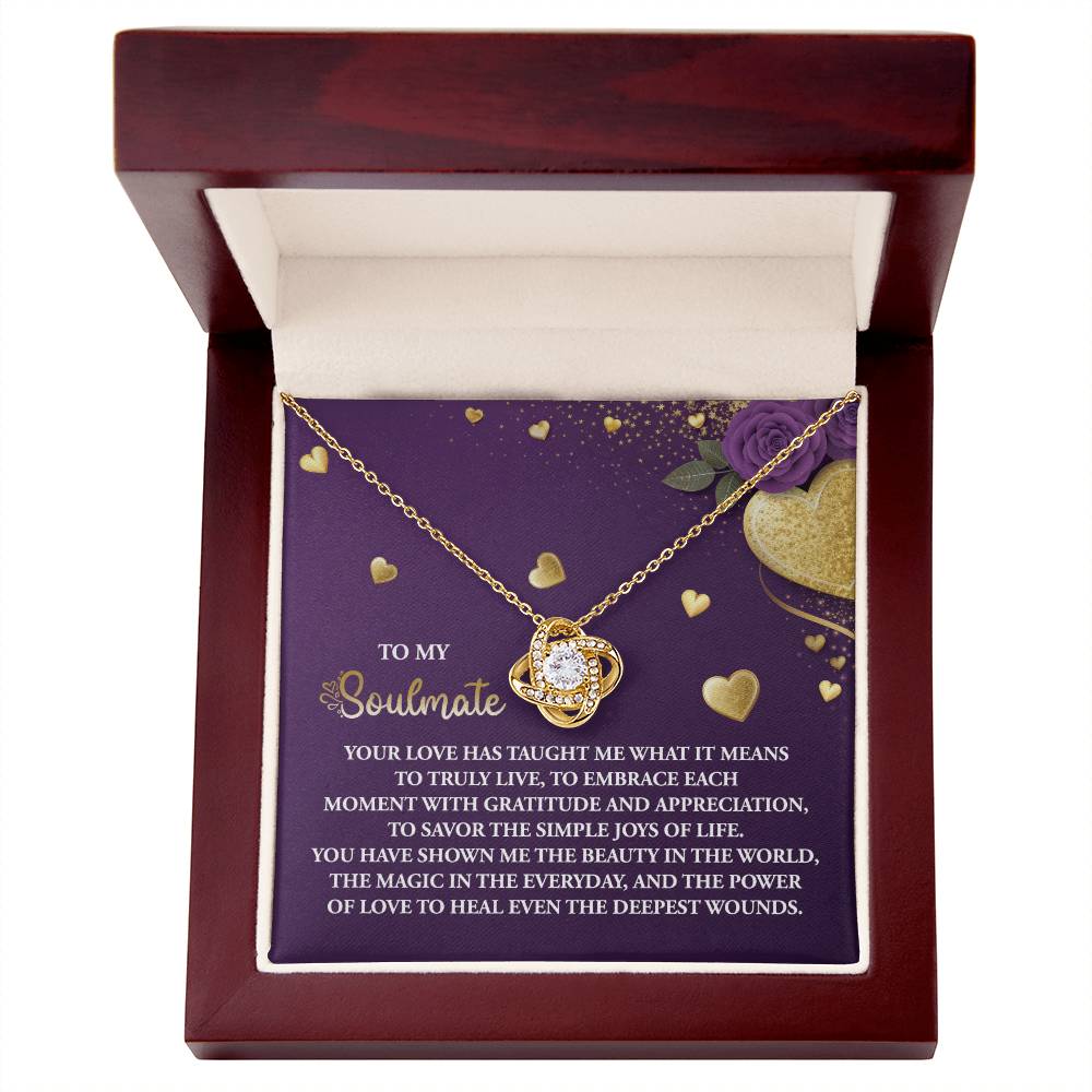 The Soulmate-Joys Of Life Love Knot Necklace features sparkling cubic zirconia crystals and is elegantly displayed in a wooden box. It includes a heart-shaped pendant and a romantic message inside, surrounded by hearts and floral designs, available in white gold or yellow gold finish.