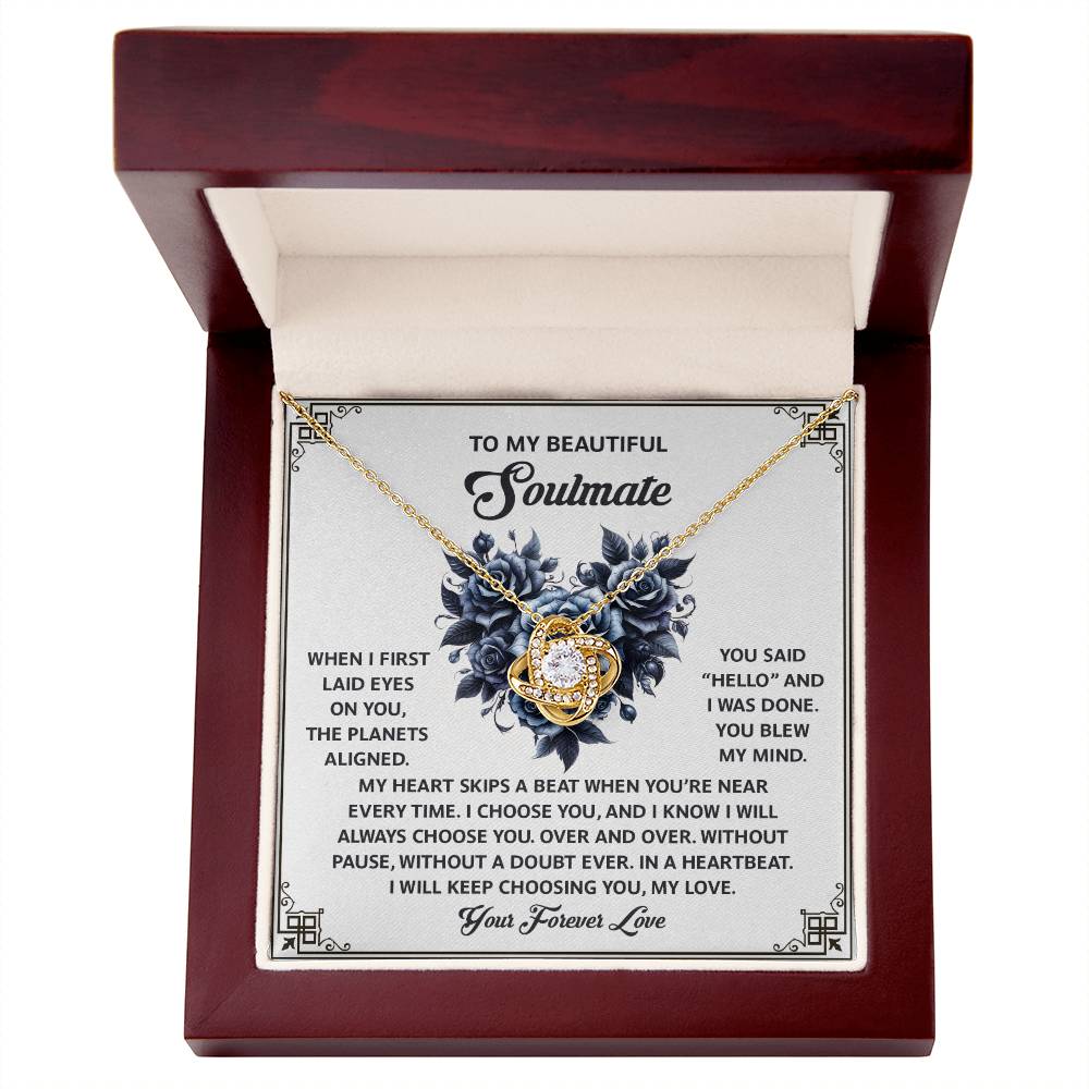 The Soulmate-Skips A Beat - Love Knot Necklace, featuring a floral design and adorned with cubic zirconia crystals, is showcased in a wooden box. The box's lid bears an inscription about love for a soulmate.
