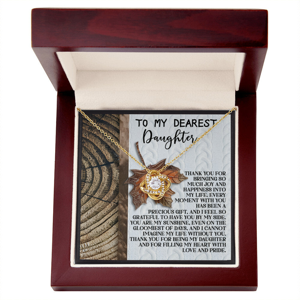 The Daughter-Love And Pride - Love Knot Necklace, featuring a sunflower pendant adorned with cubic zirconia crystals, is beautifully presented in an open wooden box. The lid of the box contains a heartfelt message addressed to a daughter.