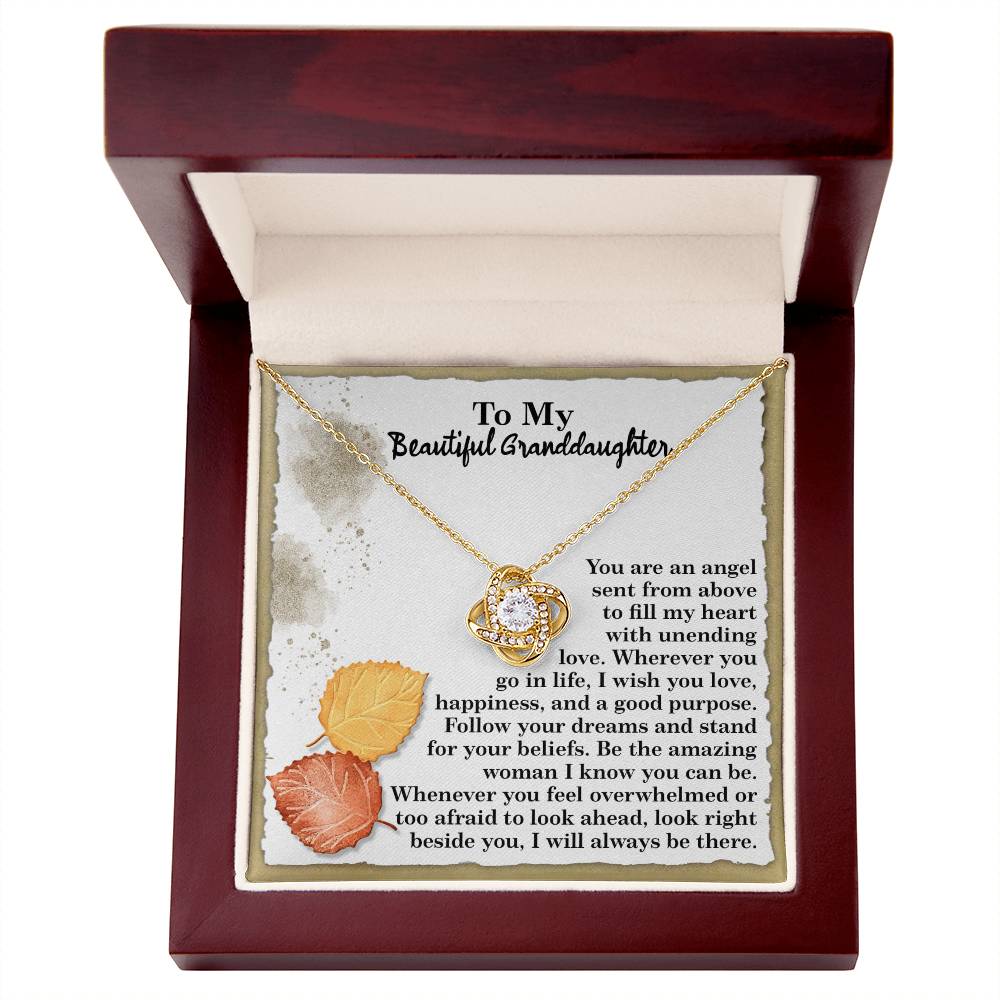 The Granddaughter-An Angel - Love Knot Necklace features a beautiful circular pendant, elegantly presented in a box. It is crafted with a white gold finish and adorned with sparkling cubic zirconia crystals, carrying a heartfelt message for a granddaughter and highlighting intricate autumn leaves in its design.