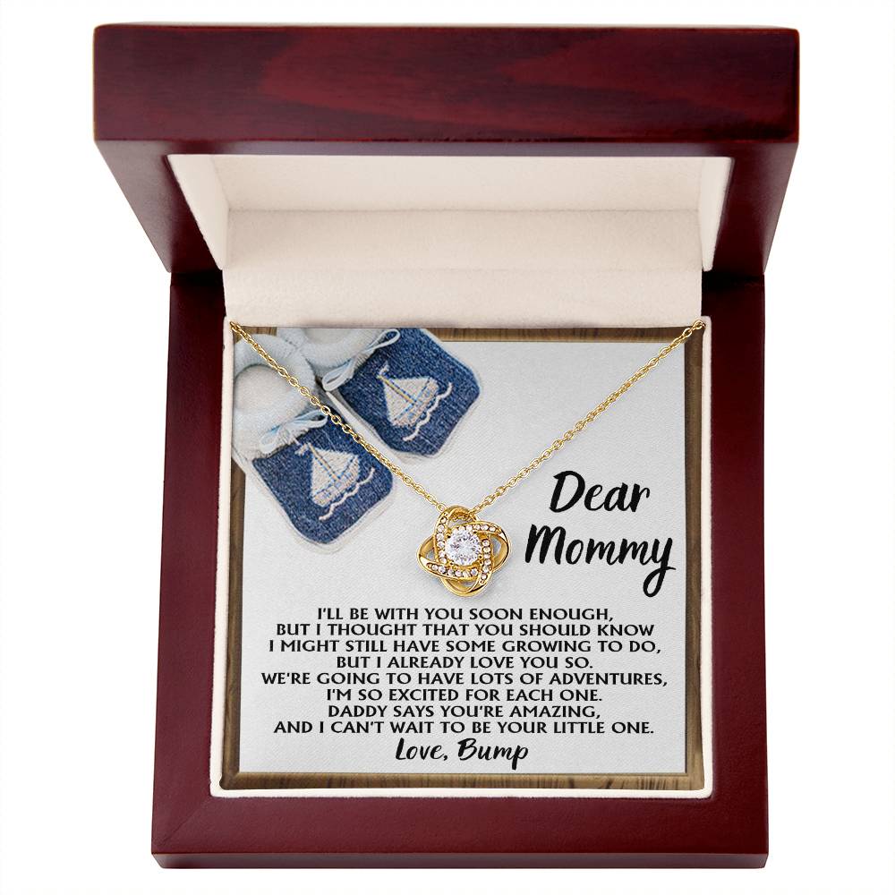 A jewelry box containing the "To Mom To Be, You're Amazing - Love Knot Necklace," crafted from 14k white gold and featuring a gemstone pendant. The interior of the box displays a heartfelt message from a baby to "Mommy," expressing excitement for future adventures. Decorated with cubic zirconia crystals, this keepsake embodies love and cherished memories.