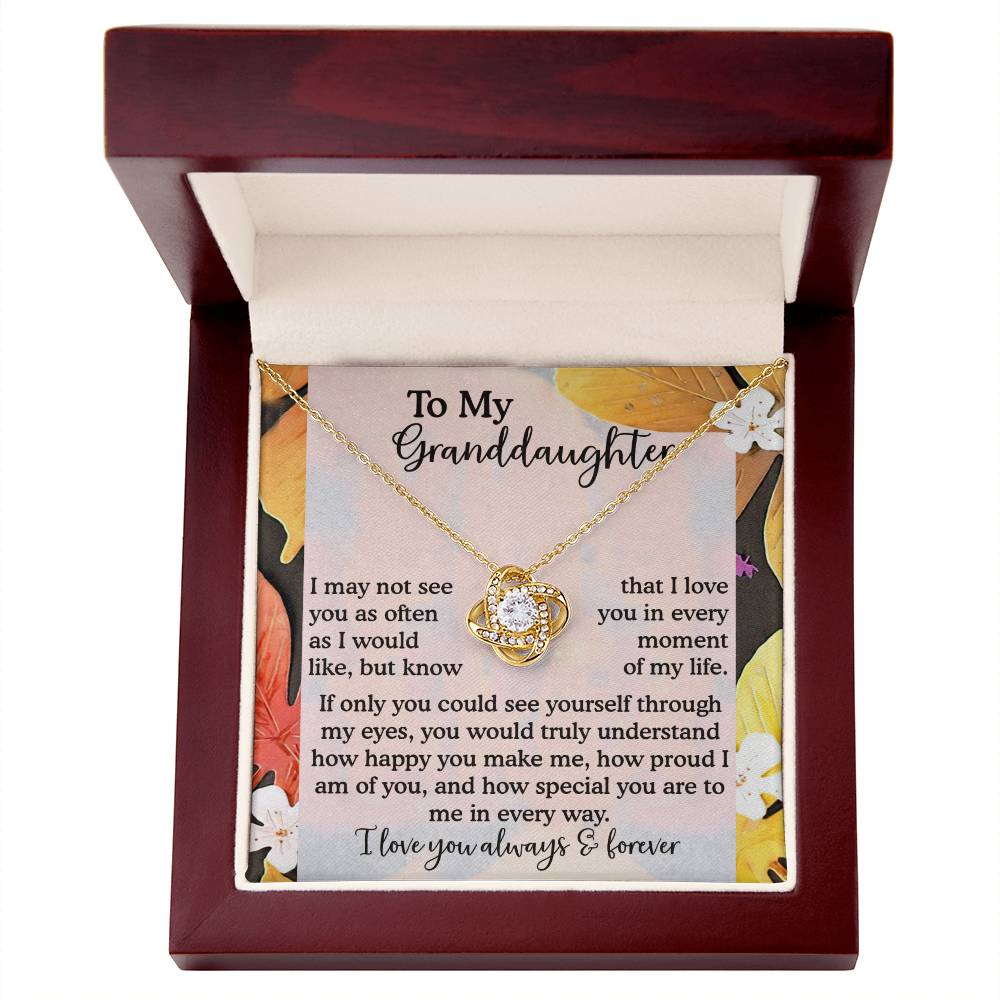 The "Granddaughter-In Every Way - Love Knot Necklace" features a circular pendant embellished with cubic zirconia crystals, all elegantly presented in a red jewelry box. This box includes a heartfelt message for a granddaughter, enhancing the sentimental value of the necklace's stunning gold finish.