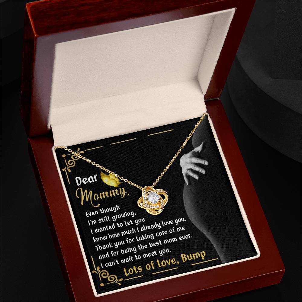 The "To Mama To Be, Best Mom Ever - Love Knot Necklace" features a heart-shaped pendant adorned with sparkling cubic zirconia crystals, available in a choice of white gold or yellow gold finishes. It comes elegantly packaged in a jewelry box, with an interior lid that displays a heartfelt message from "Bump" to "Mommy," expressing gratitude for her care and eager anticipation for their meeting.