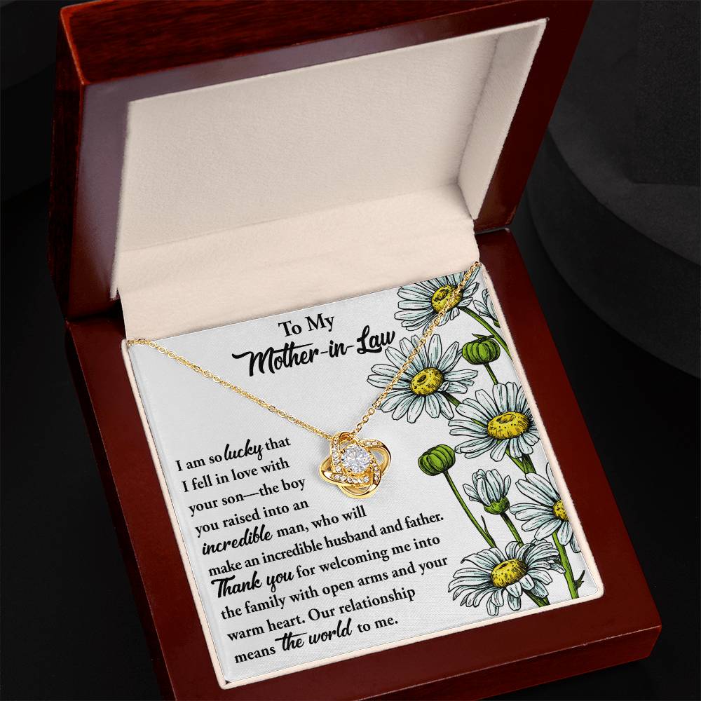 The "To Mother-In-Law, Warm Heart - Love Knot Necklace," adorned with Cubic Zirconia, placed in an open wooden box with illustrations of daisies on the side, comes accompanied by a heartfelt note expressing gratitude to a mother-in-law.