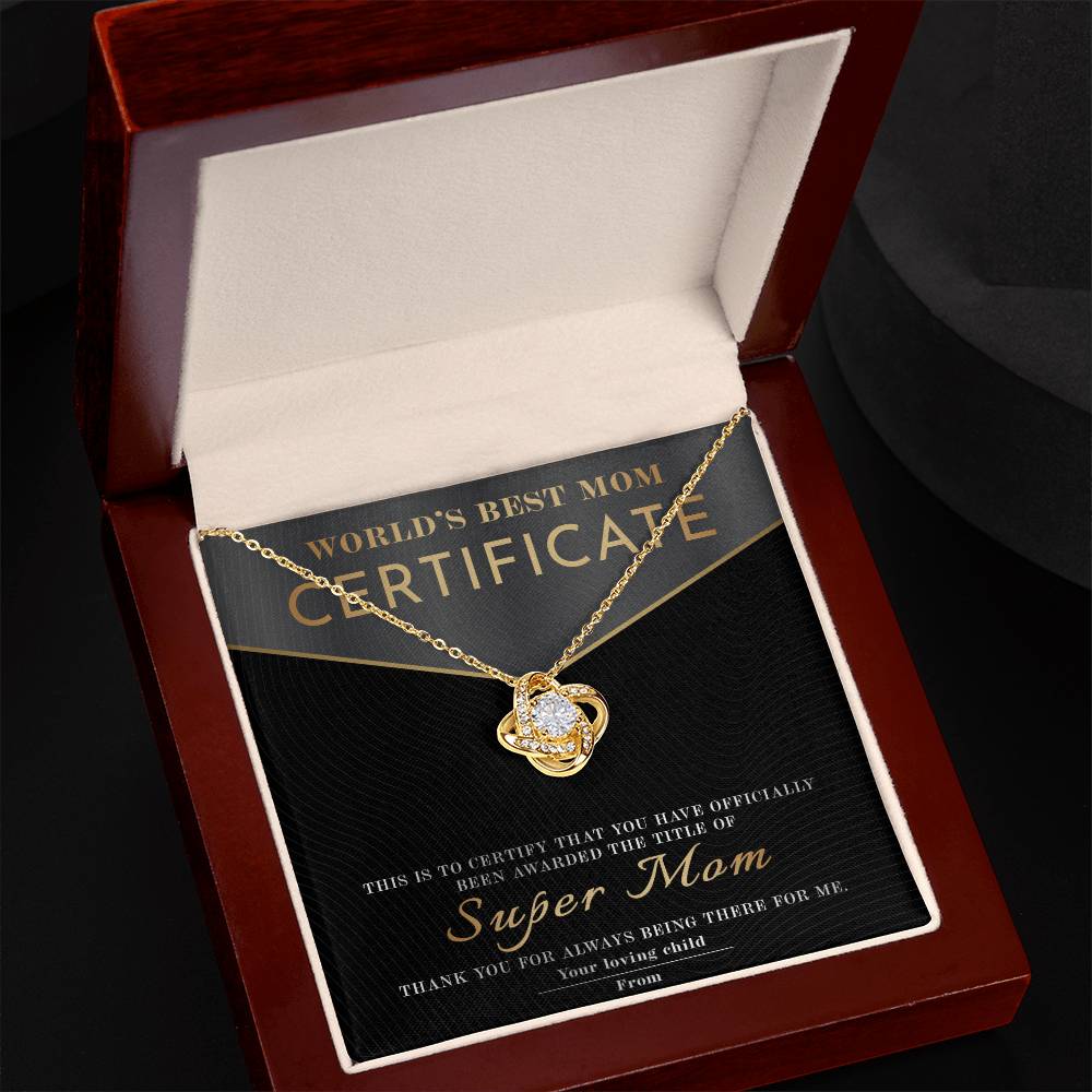 The Mom-Best Mom Certificate - Love Knot Necklace, featuring a sparkling pendant with cubic zirconia, is beautifully presented in an open jewelry box. Behind it sits a "World's Best Mom Certificate," honoring her as "Super Mom" from a grateful child—an ideal personalized gift.