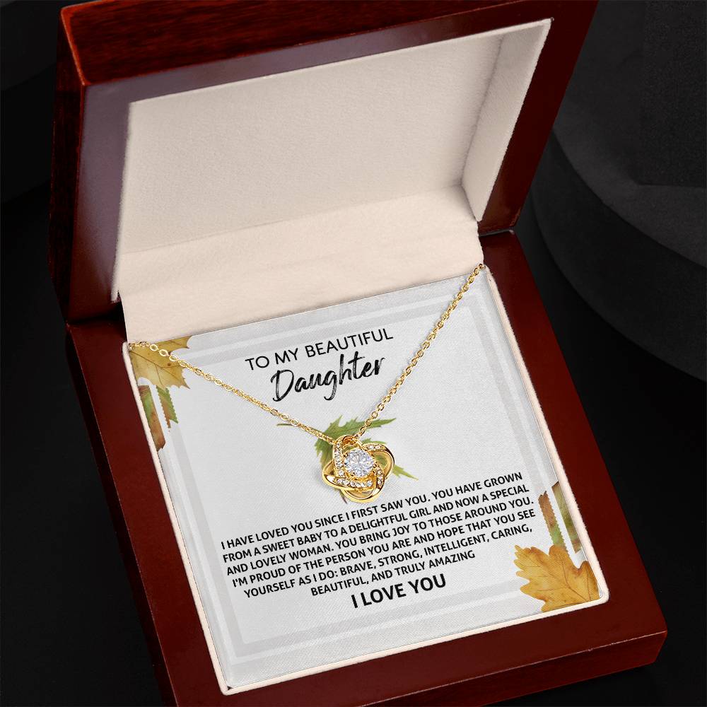 A personalized gift, the Daughter-See Yourself - Love Knot Necklace showcases two interlocked hearts adorned with cubic zirconia crystals, presented on a message card reading "To My Beautiful Daughter" inside a wooden jewelry box.
