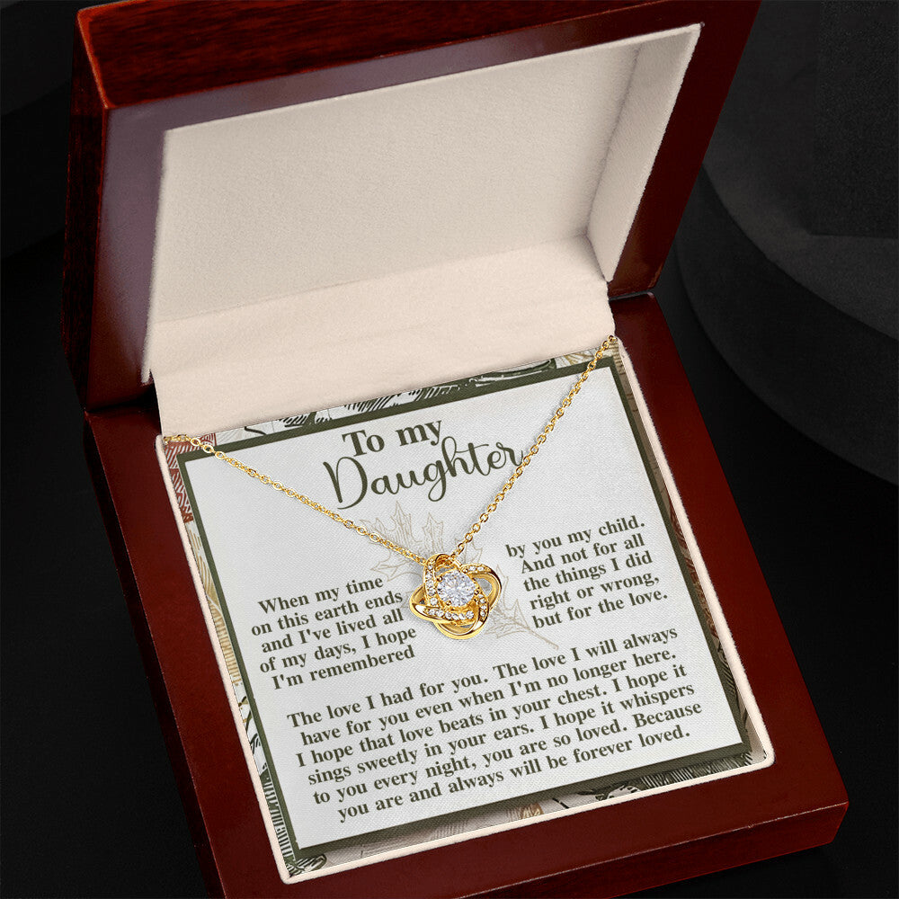 A Love Knot Necklace, featuring interlocking hearts and adorned with sparkling cubic zirconia crystals, is showcased in an open wooden box. The box includes a heartfelt message addressed "To my Daughter.