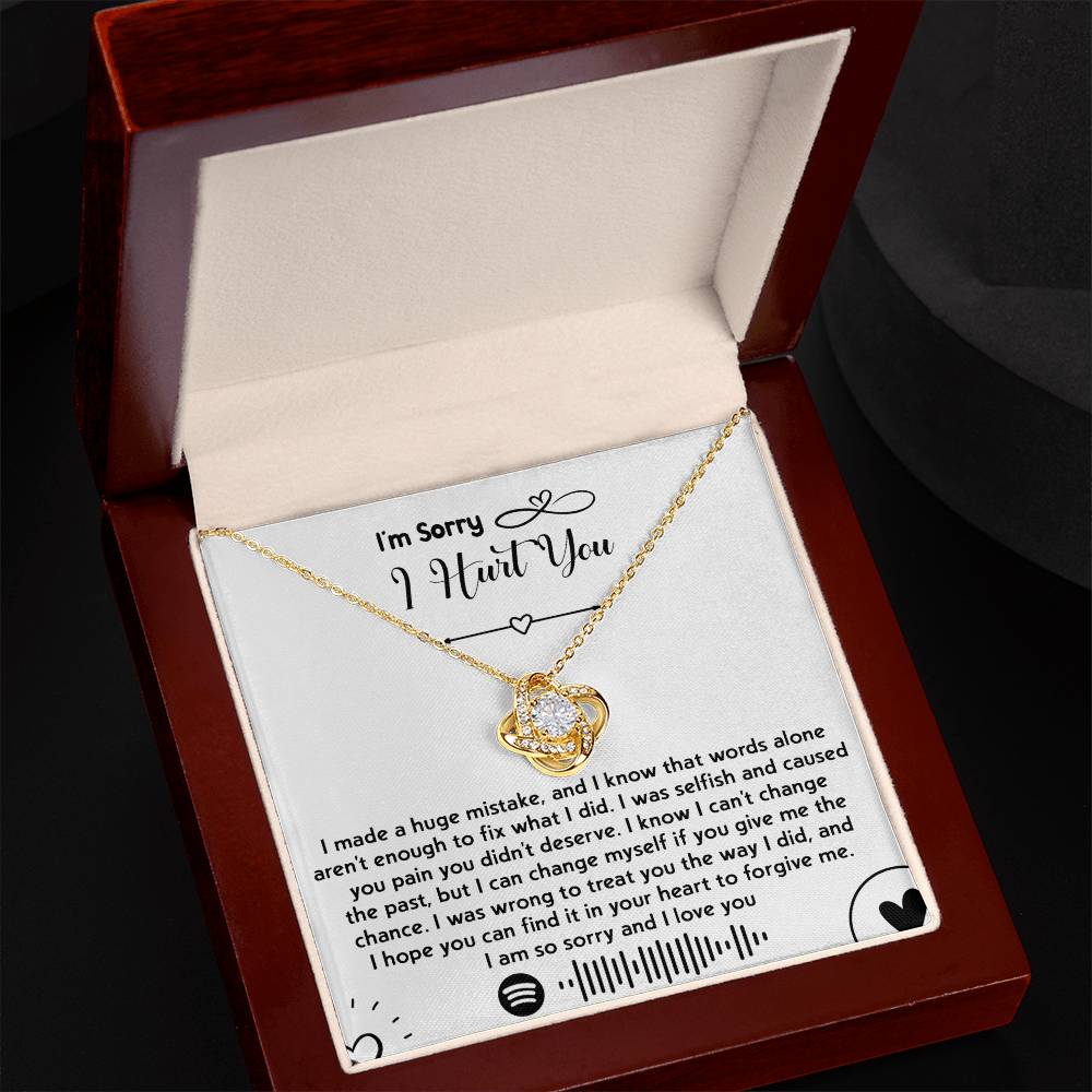 A "Sorry-You Didn't Deserve - Love Knot Necklace" with a heart-shaped pendant adorned with premium cubic zirconia crystals rests in a jewelry box. Behind the necklace, a printed apology note expressing deep regret and seeking forgiveness adds a heartfelt touch.