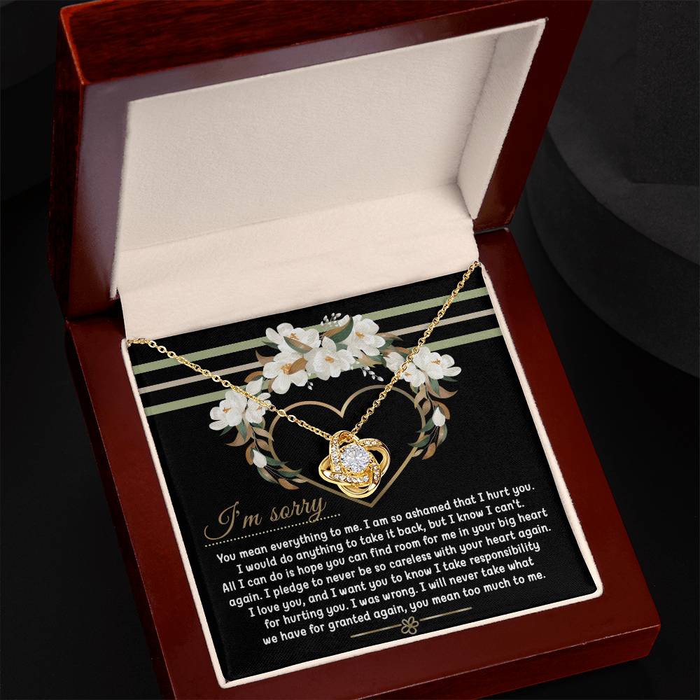Introducing the Sorry-Big Heart - Love Knot Necklace: a heart-shaped pendant nestled in an elegant box, complete with an apology message expressing love and regret for causing hurt. The backdrop showcases a beautiful floral heart design, while the pendant sparkles with cubic zirconia crystals. Personalize your necklace by choosing between a white gold or yellow gold finish.