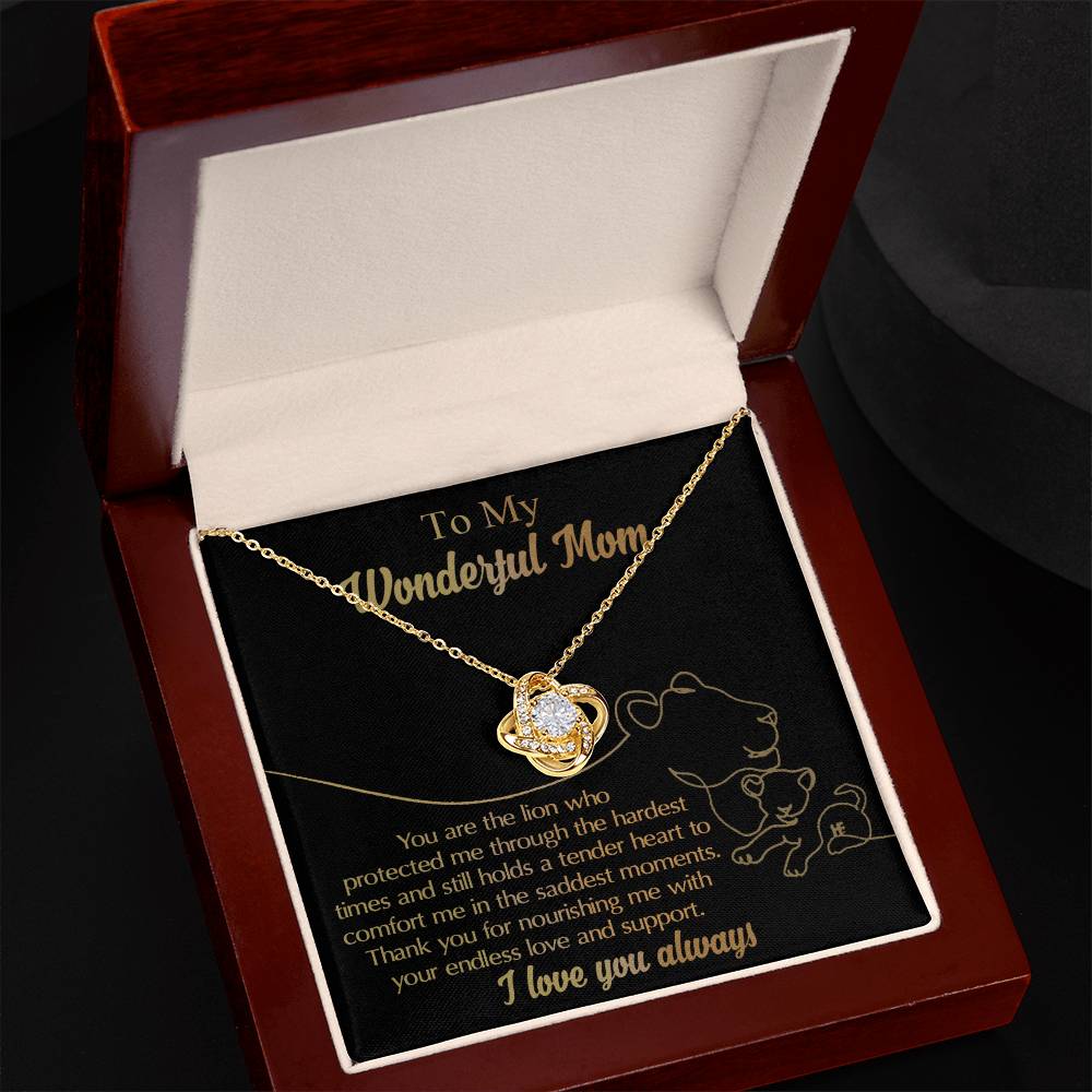 A To Mom, The Lion - Love Knot Necklace featuring a heart-shaped pendant sits inside an open jewelry box. The box includes a heartfelt message dedicated to a mother, and the necklace sparkles with cubic zirconia accents.