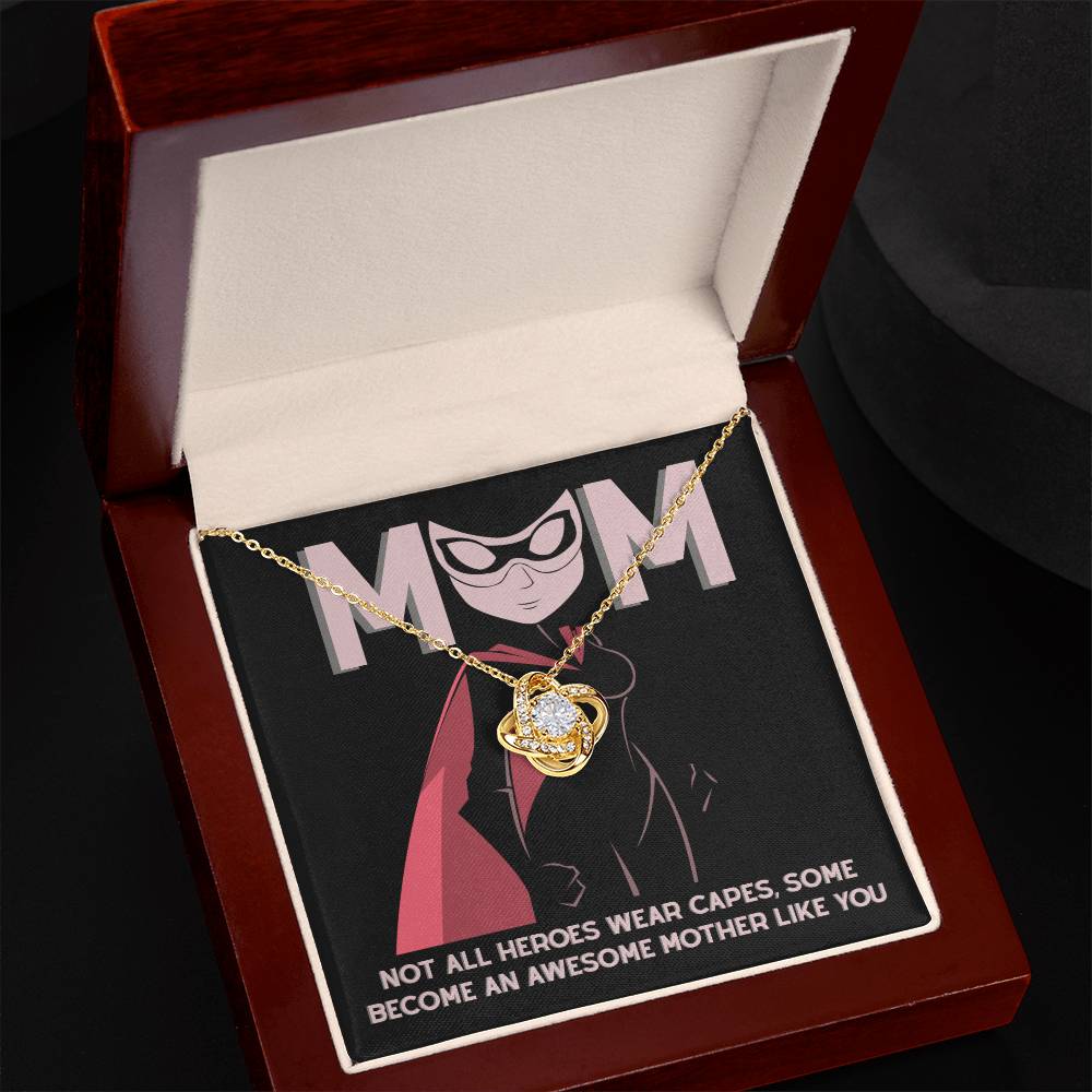 The Mom-An Awesome Mother - Love Knot Necklace, with a gold finish and cubic zirconia crystals, comes in a wooden box alongside a superhero-themed card that reads: "MOM" and "Not all heroes wear capes. Some become an awesome mother like you.