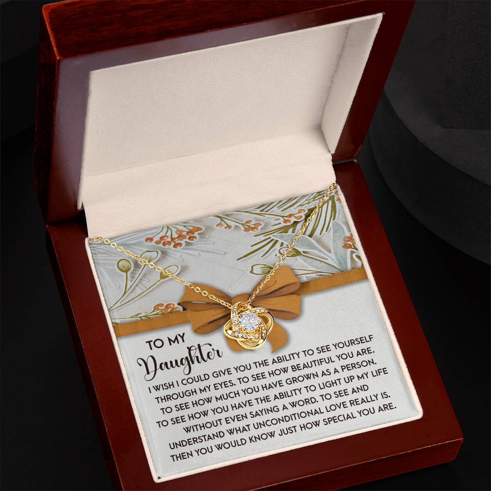 The Daughter-Saying A Word - Love Knot Necklace, embellished with dazzling cubic zirconia crystals, is nestled in a jewelry box. Its heart pendant holds deep significance, showcasing an interlocking design and a heartfelt message dedicated to a beloved daughter, making it the ideal personalized gift.