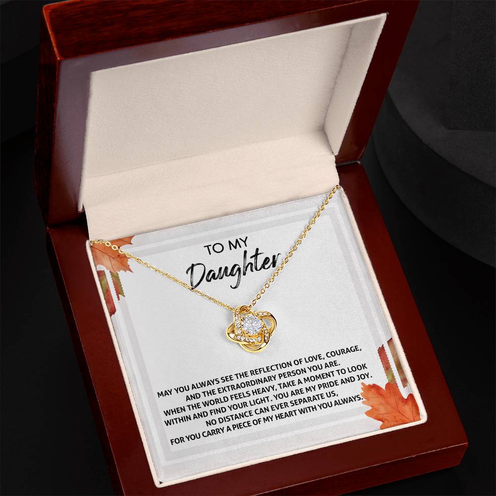 The Daughter-Find Your Light - Love Knot Necklace, adorned with a heart pendant featuring cubic zirconia crystals, rests inside an open wooden jewelry box. The box's lid displays a heartfelt message for a daughter.