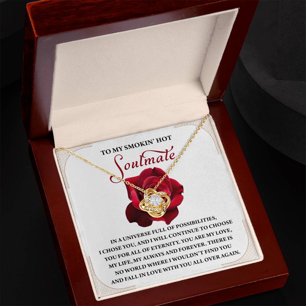 The Soulmate-Over Again - Love Knot Necklace, adorned with intertwined hearts and cubic zirconia crystals, rests in an open jewelry box. It includes a heartfelt message for a soulmate and is beautifully framed by a single red rose in the background.
