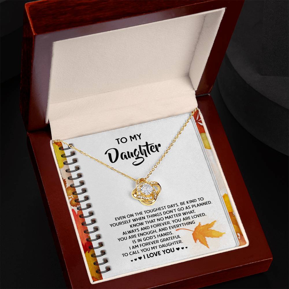 A jewelry gift box containing the "Daughter-In God's Hands - Love Knot Necklace," adorned with cubic zirconia, and a card that reads, "To My Daughter" along with an inspirational message inside. This personalized gift beautifully captures your heartfelt sentiments.