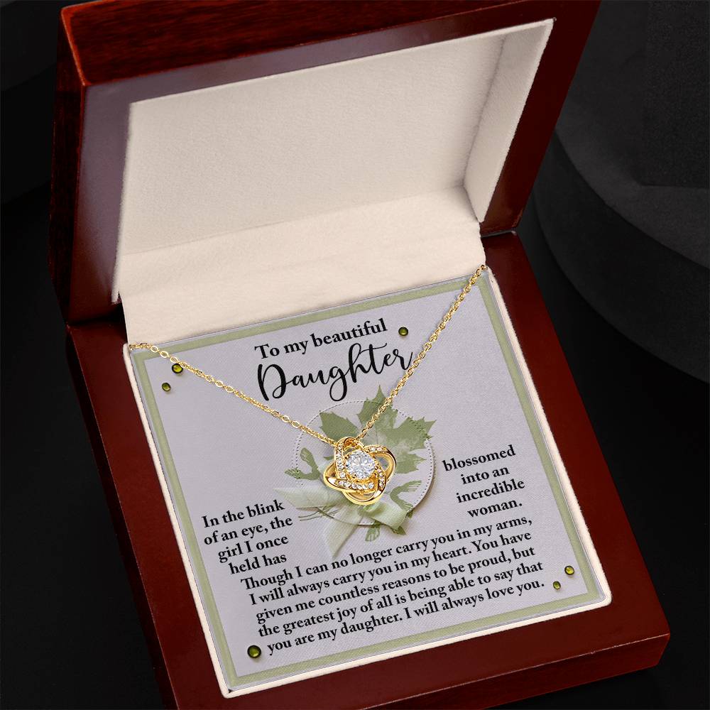 A Love Knot Necklace with a gold finish sits in an open jewelry box. Inside the lid, there is a sentimental message addressed "To my beautiful Daughter." The delicate pendant sparkles with cubic zirconia crystals, reflecting the love and care put into this special gift named the Daughter-Incredible Woman.