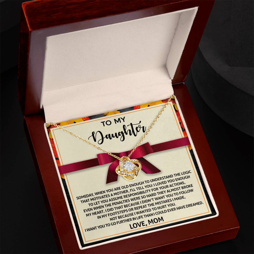 A Daughter-Further In Life - Love Knot Necklace, featuring a heart-shaped pendant adorned with cubic zirconia crystals, is elegantly displayed in an open wooden box. The inside lid bears a heartfelt note addressed "To My Daughter, Love, Mom.