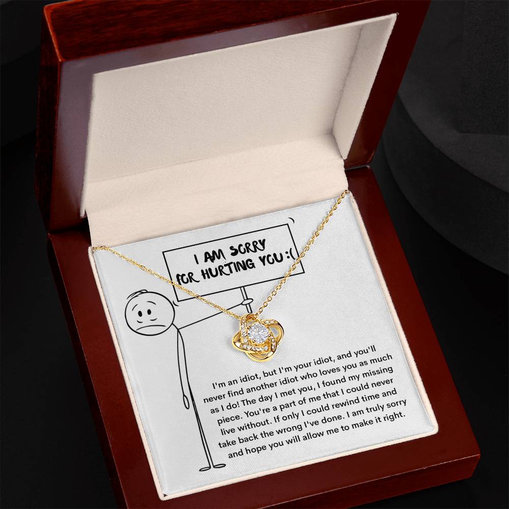 The Sorry-Missing Piece - Love Knot Necklace, adorned with cubic zirconia crystals, sits in an open jewelry box. The box contains a note with an apology message and a stick figure holding a sign that reads, "I am sorry for hurting you.
